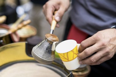Eller sıcak kum ve dökülen bakır turk tek kullanımlık kağıt bardak içine adam yapma geleneksel Türk kahve close-up. Kahve Arapça hazırlık kavramı