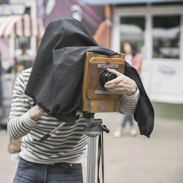 Photographer with vintage wooden camera under dark cloth cape, photographing clients, artifact, antiquity