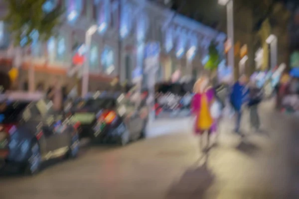 Background on city street at night, motion effect. Abstract blurred silhouette of girl in bright raincoat walking alone. Seasons, weather, modern women concepts
