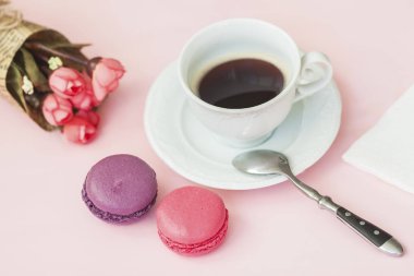 Pembe ve vioet macarons, bademli kurabiye, buket bahar çiçek ve fincan kahve, kaşık, üstten görünüm. Romantik sabah, sevgili için hediye