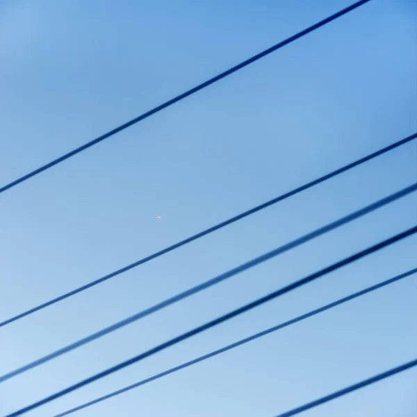 Электрические провода и крошечный самолет высоко в небе — стоковое фото