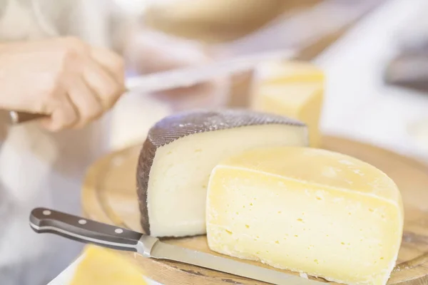 Cheese heads no balcão do mercado, vendedor vende queijo, cortar cabeças de queijo na placa de madeira do mercado. Foco seletivo. Produtos lácteos gastronómicos, cena real, mercado alimentar — Fotografia de Stock