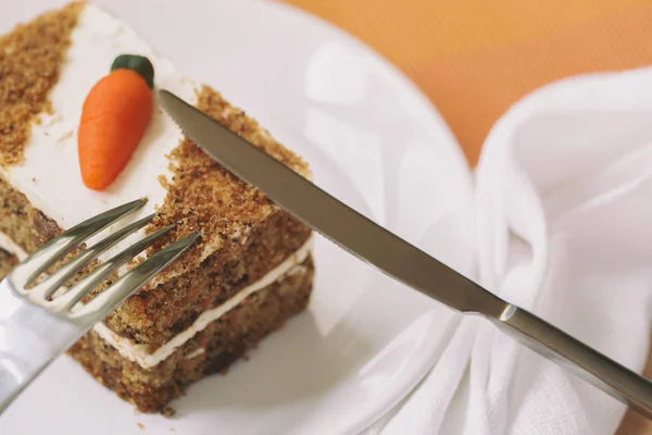 Homemade carrot cake with carrot decorations, slice on white plate close-up, fork, knife, selective focus, copy space