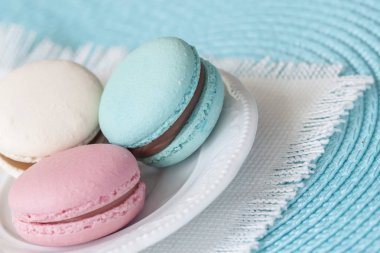 Farklı renkler ve farklı tatlar beyaz tabak, beyaz vintage peçeteye üç macaroons.
