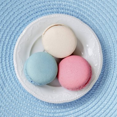 Üç macaroons farklı renkler ve beyaz bir tabak, üstten görünüm içinde farklı tatlar. Kare arka plan