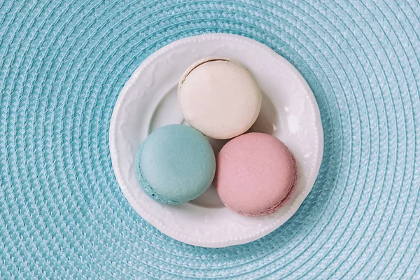 Tres macarrones de diferentes colores y diferentes gustos en un plato blanco, vista superior. Mañana romántica, regalo para la amada. Desayuno en San Valentín, Madres, Día de la mujer — Foto de Stock