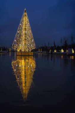 Açık metal ladin ağaçları ve onun ıslak kaldırımda yansıması, neon ışıklı inşaat. Şehir ışık dekoru. Noel ve Yeni Yıl dekorasyonları