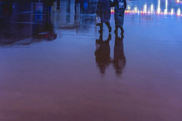 Silhuetter av abstrakta unga och äldre kvinna skyndar i regnet tillbaka till oss, deras reflektion i våt asfalt, i en pöl, begreppet årstider, väder, livsstil — Stockfoto