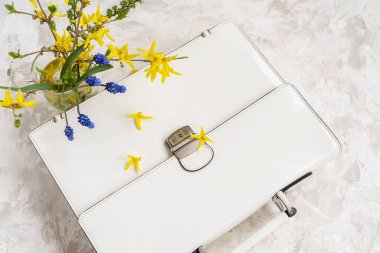 Parlak çiçeklerle dolu bir buketin yanında duran beyaz evrak çantası, üst manzara. Bahar ya da yaz alışverişi, iş ve romantizm kavramı, okula dönüş, anne tatili