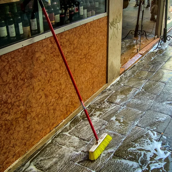 Venice, Italy - February 28, 2012: Cleaning the sidewalk with a brush and soap in front of the entrance to the liquor store.