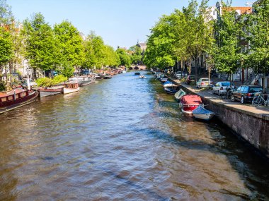 Amsterdam 'daki su kanalı. Rıhtım, çeşitli binalar, arabalar, yatlar ve tekneler. Güneşli.