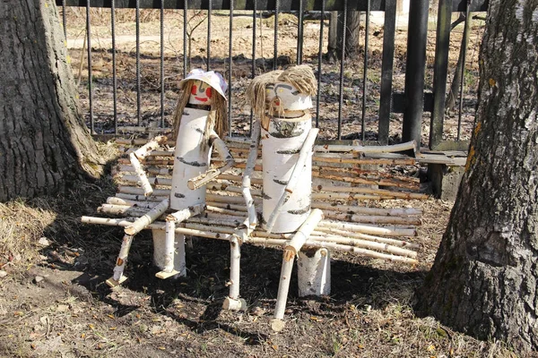 Duas figuras de madeira de pessoas sentadas em um banco na rua em um dia de verão. Feito à mão. Decoração rural . — Fotografia de Stock