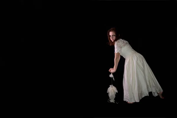 Young woman in white wedding dress and a lace umbrella stands barefoot against a black background — Stock Photo, Image