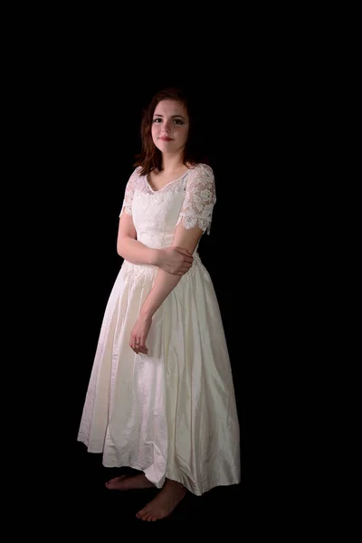 Young woman in white wedding dress stands barefoot against black background — Stock Photo, Image