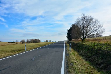 Rhoen, Bavyera, Almanya 'da mavi gökyüzü olan yeşil bir arazide yalnız bir yol.