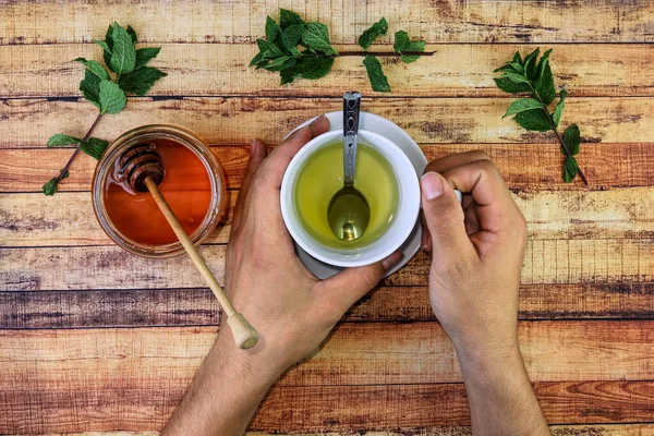 Sick man holds hot herbal tea for warms hands. Good raws also is brown honey, mint leaves and important allowance lemon. Modern apothecary, self-care, immunity. Basic things for sickness — Stock Photo, Image
