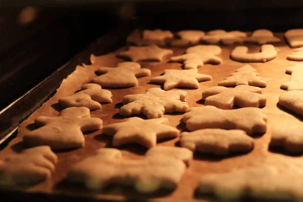 Mujer mira cómo hornear galletas de Navidad y sacarlas del horno. Los personajes de pan de jengibre se hornea a color dorado para un sabor grande y crujiente. Concepto de unión y vacaciones de invierno —  Fotos de Stock