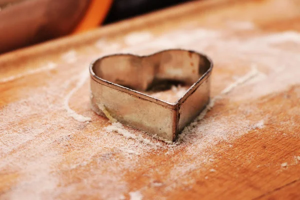 Metal heart for christmas cookies. Baking with family. Spending a few minutes with special person. Concept of winter holidays, teamwork and others feelings. Wooden board sprinkled with flour