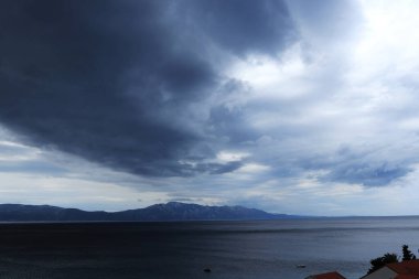 Neretvanski kanal 'daki Split-Dalmatia ilçesine fırtına yaklaşıyor. Fırtınalı denizi ve ağır bulutları görmek yıldırım ve yağmur getirir. Gökyüzünde mavi gölgeler ve güneş ışınları.