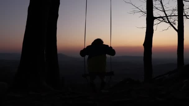 チェコ共和国のベスキディにあるプラシバ山の頂上にある特別な木製のスイングで若い男がスイングします スポーツマンは 日没時にチェコの風景に自由 新鮮な空気と景色を楽しんでいます 男の振れのシルエット — ストック動画