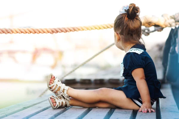 Egy kislány, egy kék ruhát a rakparton, a tengerre néző. Hajóval a háttérben. — Stock Fotó