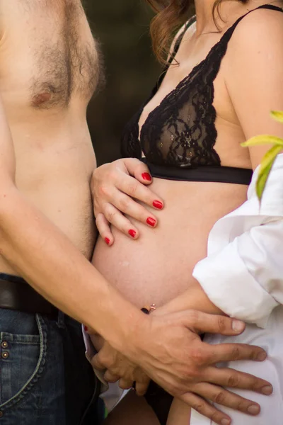 Chica embarazada abrazando su estómago, el sol brilla y la hierba verde. Concepto de mujer feliz y maternidad . — Foto de Stock