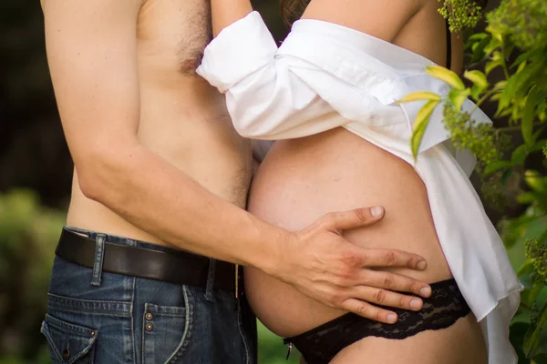 Zwanger meisje knuffelen haar maag, de zon schijnt en het groene gras. Concept van een gelukkige vrouw en moederschap. — Stockfoto