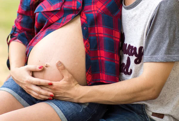 임신한 여자는 그녀의 위장, 태양이 빛난다과 녹색 잔디를 포옹. 행복 한 여자와 모성의 개념. — 스톡 사진