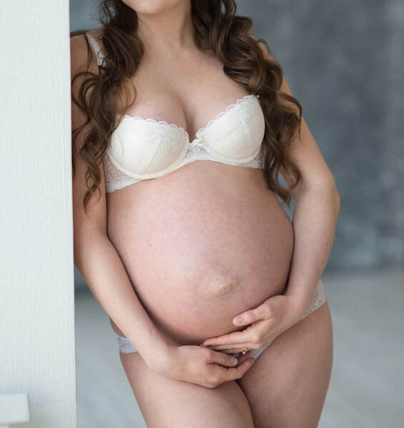 Беременная красивая молодая женщина в белых трусах обнимает живот. счастливая концепция материнства
