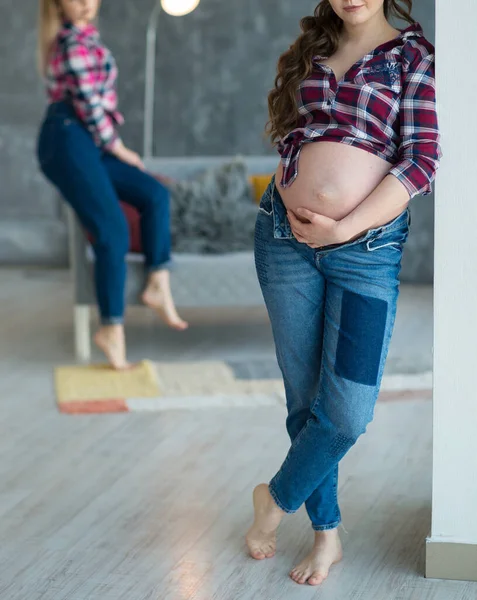 怀孕的美丽的年轻女子站在前排 坐在沙发后面 目不转睛地坐着她的朋友 快乐孕产概念 — 图库照片