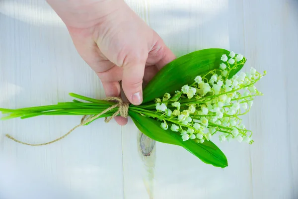 bouquet of lilies of the valley in hands on a white old wood background