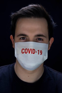 Korunmak için maske takan siyah arka planda Covid-19.baskısı olan bir adam.