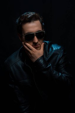 Siyah arka planda siyah deri ceketli, gözlüklü, genç seksi adam. Stüdyo çekimi