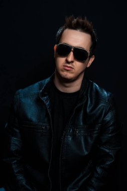 Siyah arka planda siyah deri ceketli, gözlüklü, genç seksi adam. Stüdyo çekimi