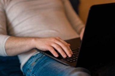 Otel odasında ya da yatak odasında dizüstü bilgisayar kullanan bir adam. Adam yatakta yatıyor ve dizüstü bilgisayarından yazıyor. Sabahları elinde modern bir aletle e-posta okuyan ve mesaj gönderen bir adam. Covid-19 salgınında uzaktan öğrenme. Özgür, uzak. 