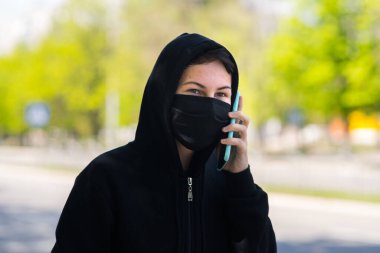 SağIık maskeli bir genç, elinde telefonla sokakta.