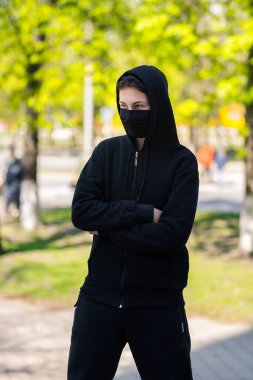 Sokaklarda maskeli bir genç. Siyah tıbbi maskeli bir adam park arka planında poz veriyor.
