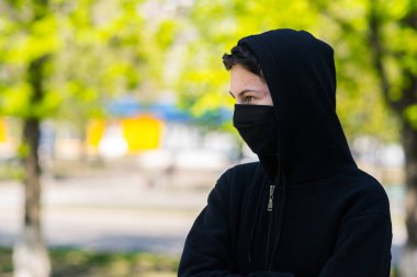 Sokaklarda maskeli bir genç. Siyah tıbbi maskeli bir adam park arka planında poz veriyor.