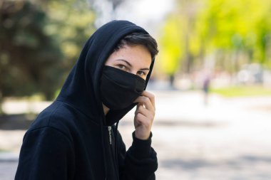 Sokaklarda maskeli bir genç. Siyah tıbbi maskeli bir adam park arka planında poz veriyor.