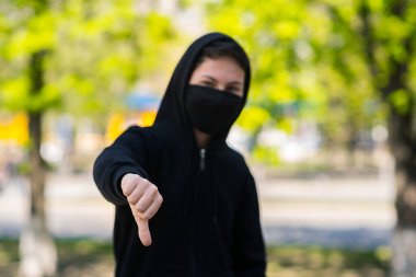 Coronavirus karantina konsepti. COVID-19. Siyah tıbbi maskeli bir genç, sağlığını grip virüsünden korur. Genç bir çocuk baş parmak hareketi yapıyor..