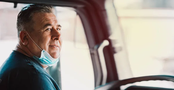 Truck driver inside the cabin with a medical mask on his face during the crisis COVID-19