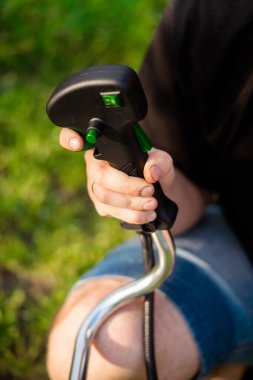 Yumuşak odaklanma. Erkek elinin işaret parmağı, çim biçmek için makinanın sapındaki yakıt ikmal düğmesine basar.