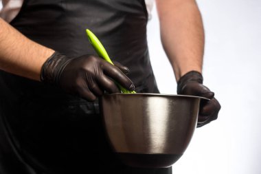 Gri arka planda izole edilmiş, gülümseyen genç bir aşçının ya da siyah önlüklü bir fırıncının görüntüsü. Yemek pişirme konsepti. Yerleşim kopyalama alanı. Kase içinde Yumurta çırpmak