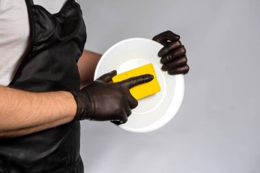 Önlüklü ve lastik eldivenli bir adam elinde temiz bir tabak ve bez tutuyor..