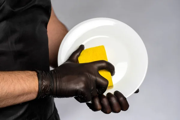 Man in apron and rubber gloves holding a clean plate and washcloth.