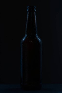 Kahverengi bira şişesi ve damlalar koyu arkaplanda etiketsiz içecek.