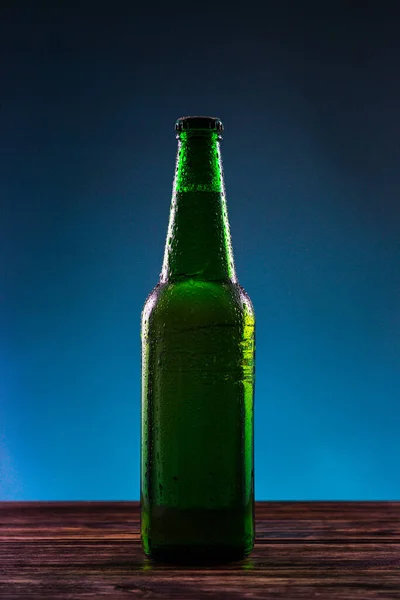 Mavi arka planda etiketsiz yeşil bira şişesi.