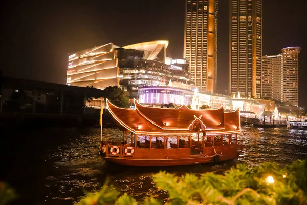Bangkok 'un gece fotoğrafı ve nehirde yüzen bir seyahat teknesi. Büyük bir şehirde akşam hayatı