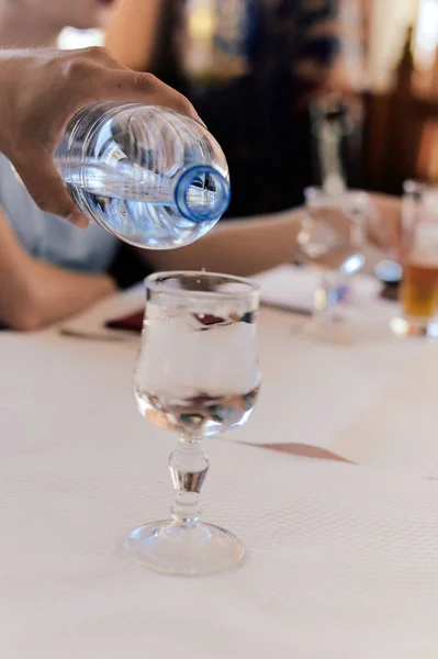 L'acqua viene versata in un bicchiere di vino su uno sfondo di luce naturale tavolo. Da vicino. — Foto Stock