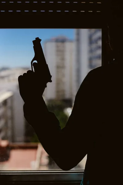 窓辺に銃を持った男のシルエット — ストック写真
